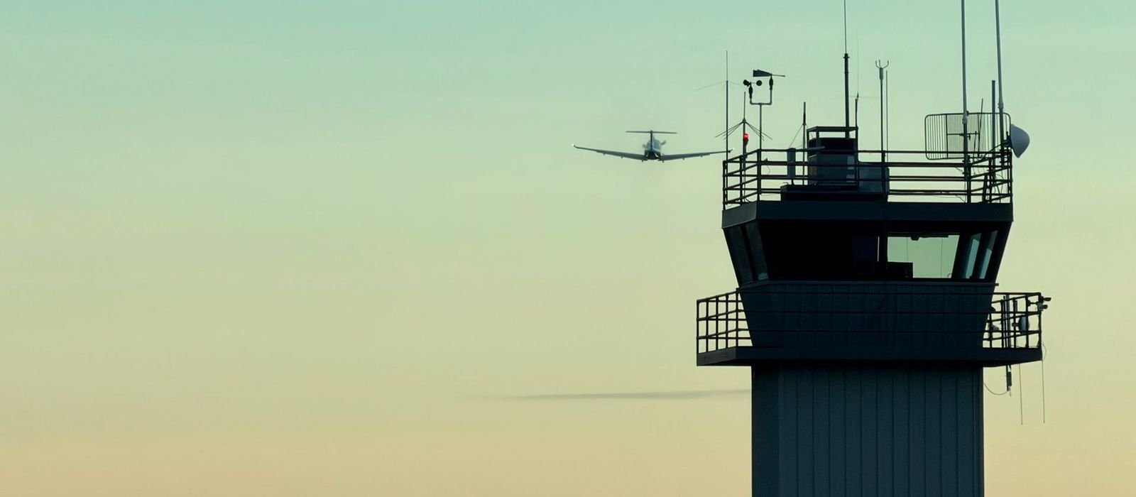 Silueta de una torre de control al anochecer con un avión
